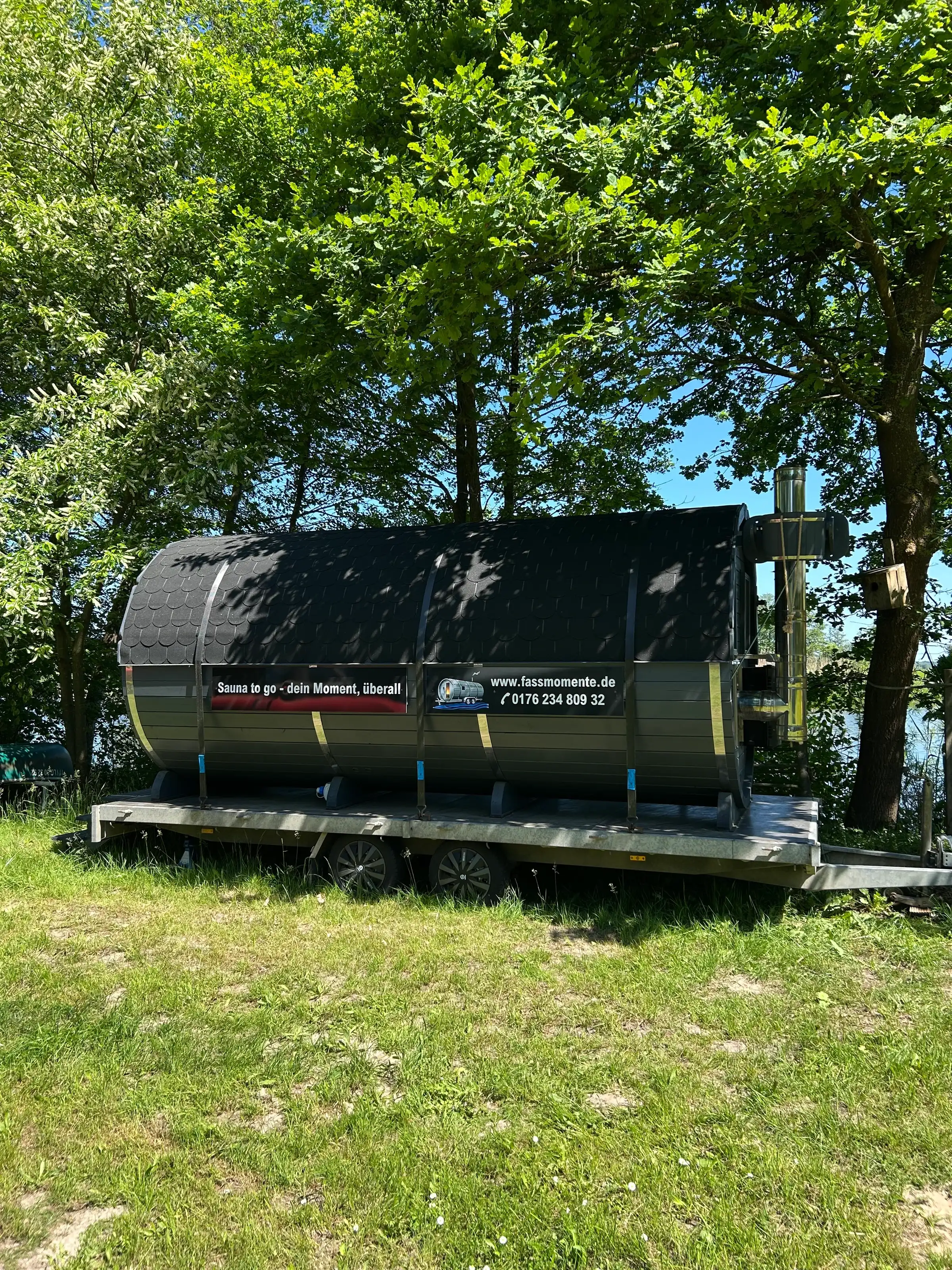 Schwarze Fasssauna auf dem Anhänger unter Bäumen