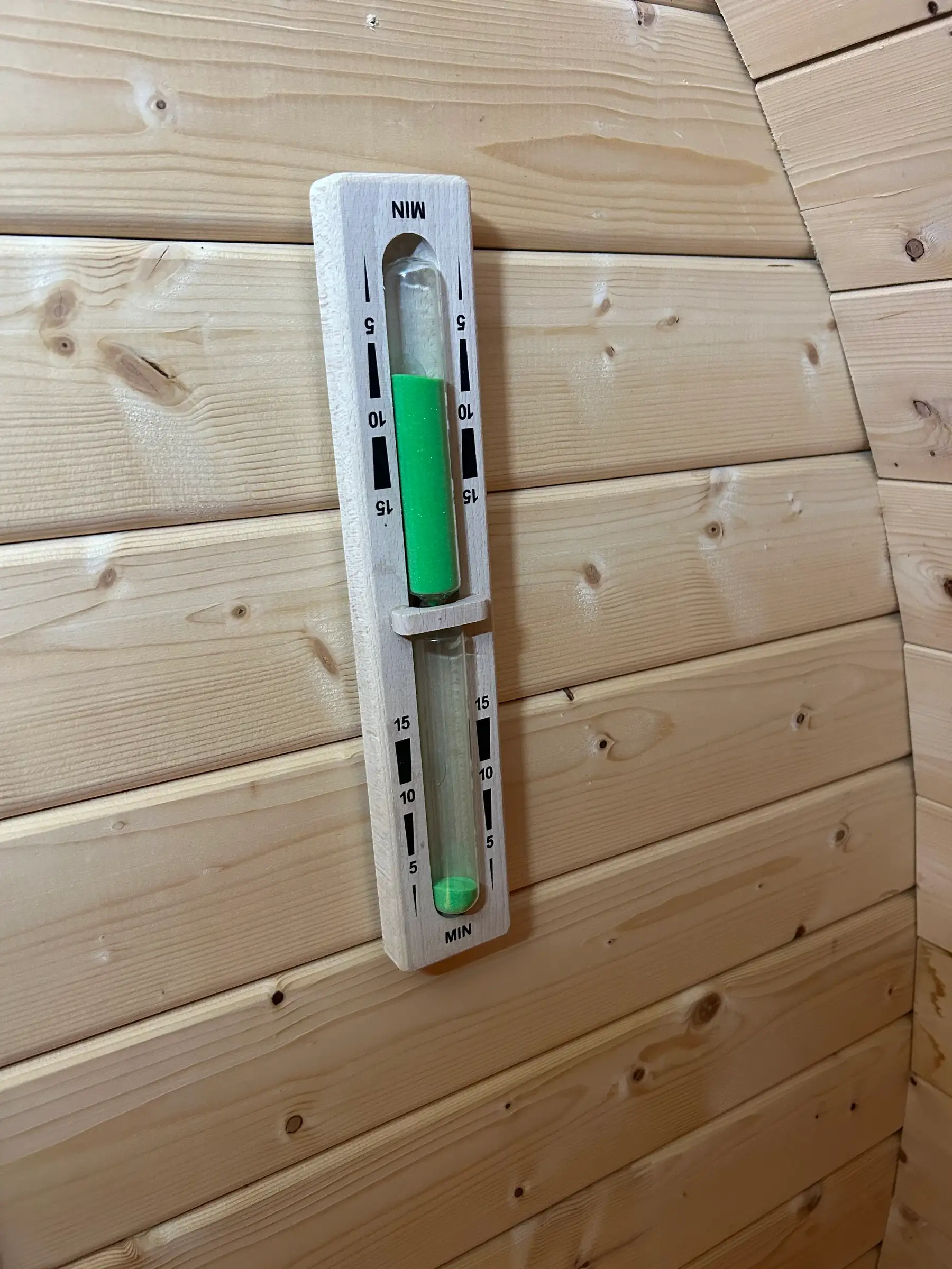 Sauna-Sanduhr aus Holz mit grünem Sand an der Holzwand der Fasssauna