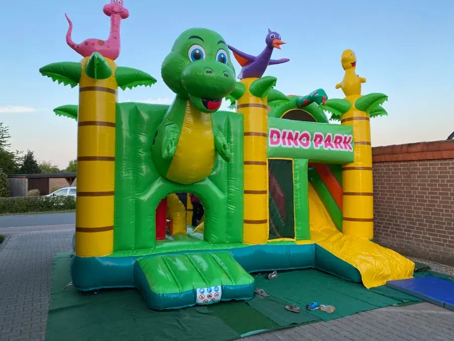 Hüpfburg Dinopark mit grünem Dinosaurier, Palmen und gelber Rutsche