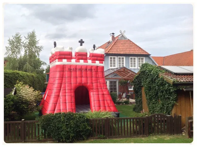 XXL-Hüpfburg Hamburg als rote Burg mit Zinnen in einem Garten